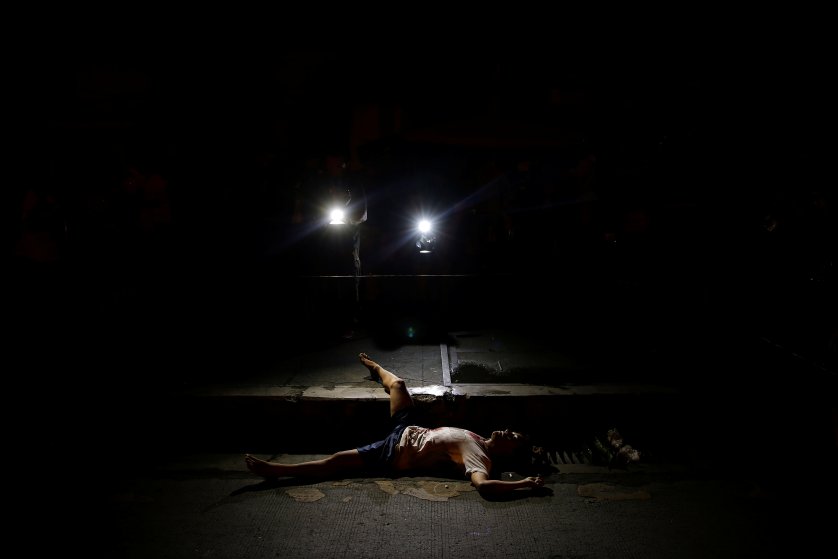 The body of a man killed by unknown gunmen is lit by lights from TV cameras in Manila