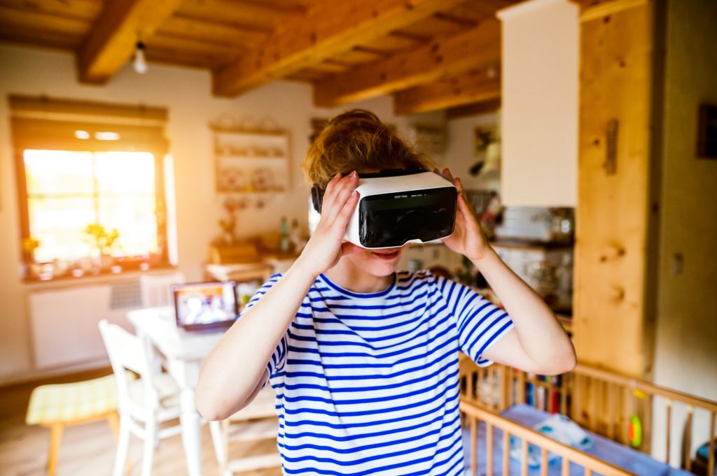Young woman in blue striped t-shirt wearing virtual reality goggles standing in living room