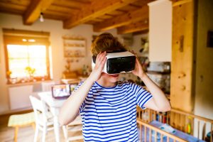 Young woman in blue striped t-shirt wearing virtual reality goggles standing in living room