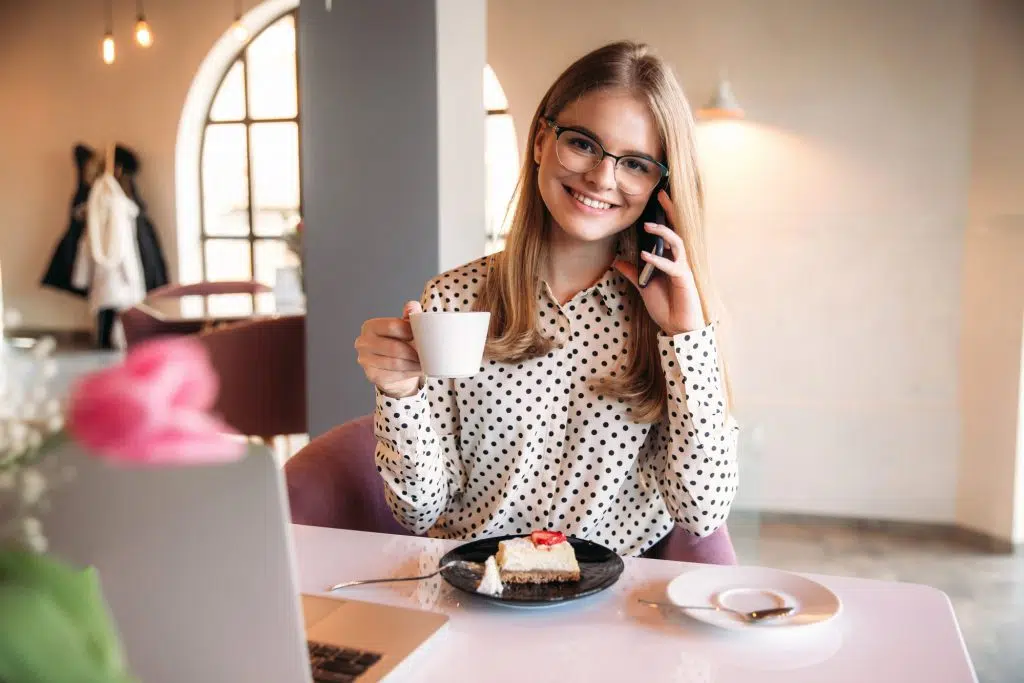 Girl eating cake in a cafe. Blonde in polka-dot shirt with laptop