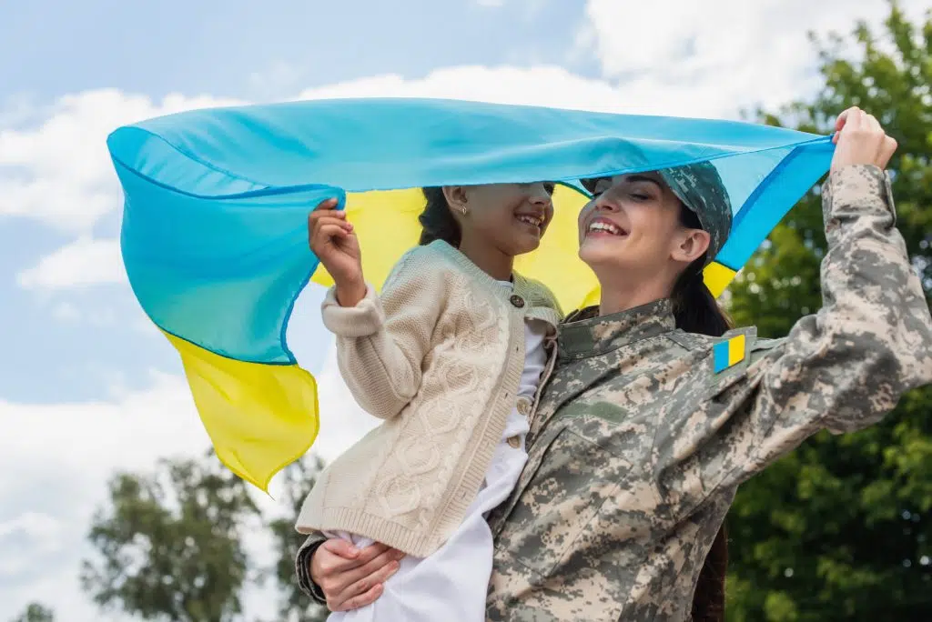 Smiling woman in camouflage holding Ukrainian flag