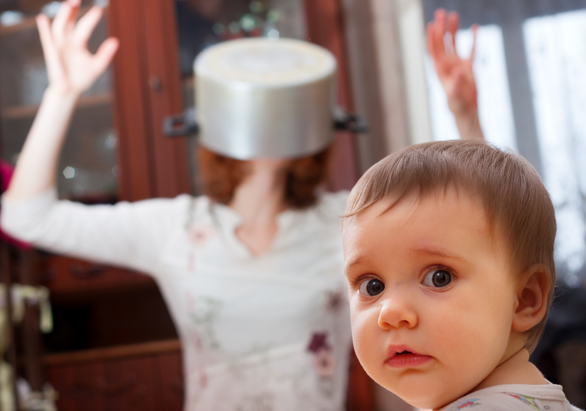 Portrait of scared baby against crazy mother with pan on head