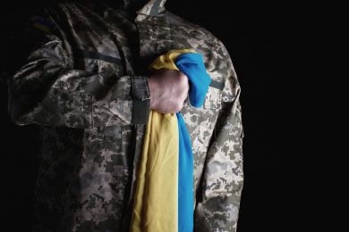 Ukrainian soldier holds in his hand the yellow-blue flag of the state, he pressed his hand to his chest,  concept of the memory of the dead soldiers
