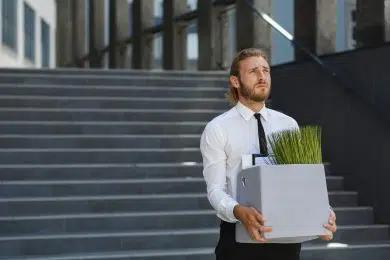 An unhappy young manager in a white shirt is fired from his job. A sad worker sits on the steps of a business center after layoffs. Crisis and unemployment