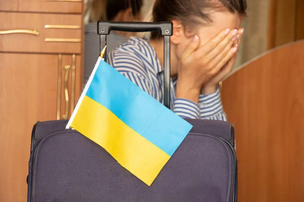 A girl cries near a suitcase with Ukrainian flags at home before leaving her home in Ukraine because of the war 2022