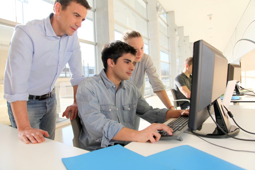 Students with teacher in front of desktop computer