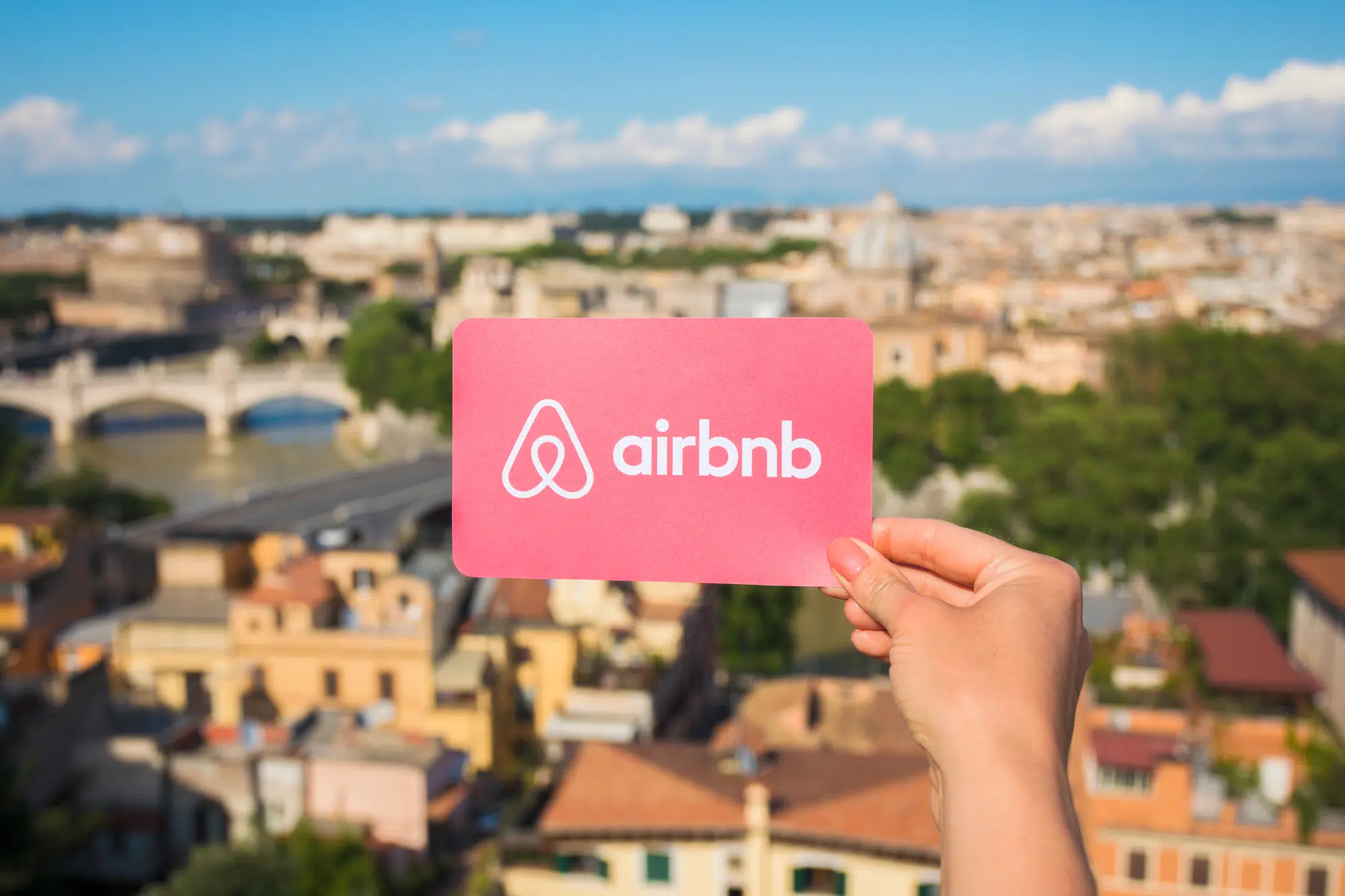 Rome, Italy - May 13, 2018: Person holding Airbnb logo in hand with city in background.