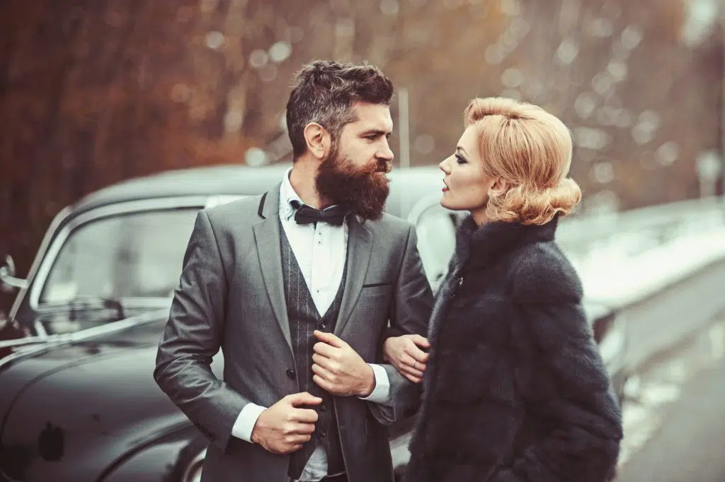 Couple in love on romantic date. Bearded man and sexy woman in fur coat. Retro collection car and auto repair by mechanic driver. Travel and business trip or hitch hiking. Escort of girl by security.