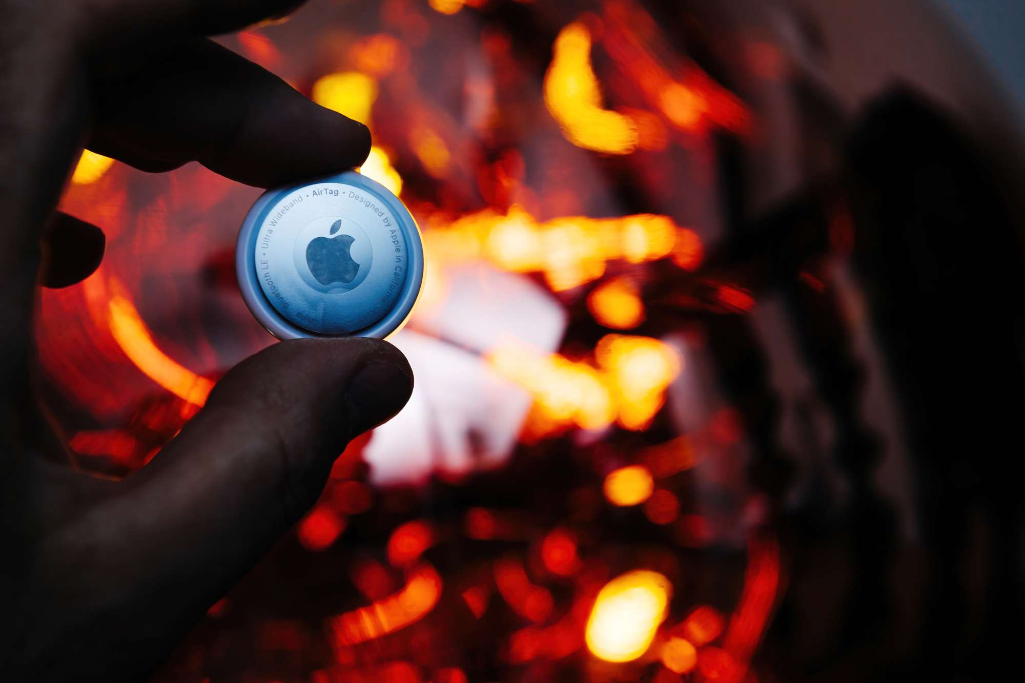 Man holding new AirTag by Apple Computers fire abstract background