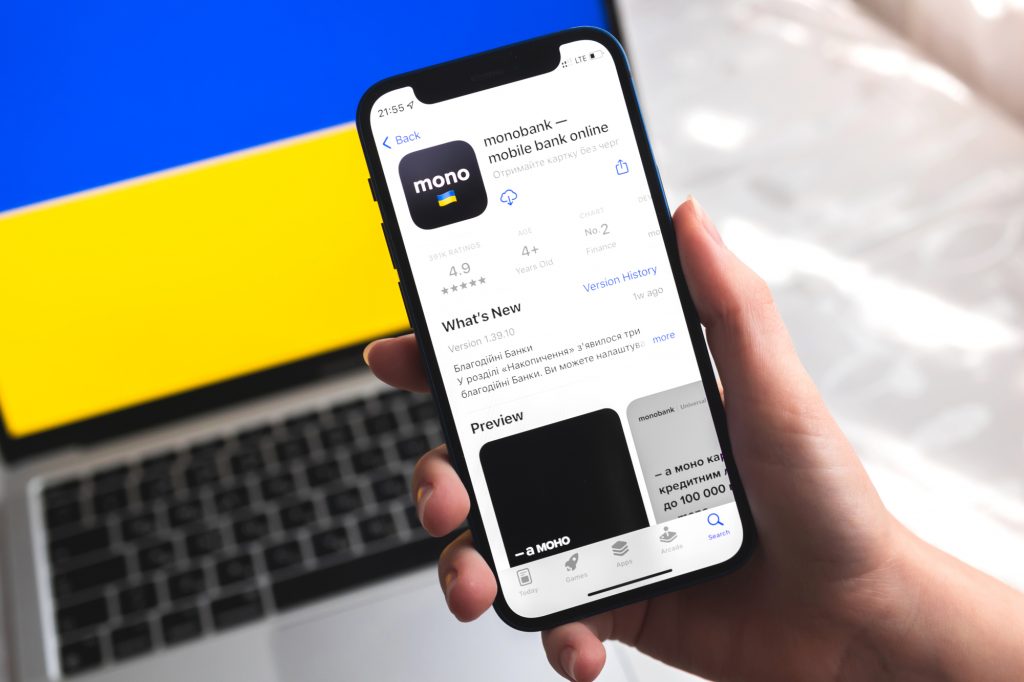 Monobank mobile banking app in Ukraine. Hand with smartphone, logo on the screen. Background with national flag
