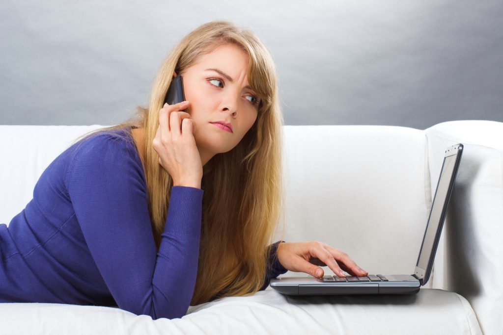 Surprised woman talking on mobile phone and looking at laptop, modern technology
