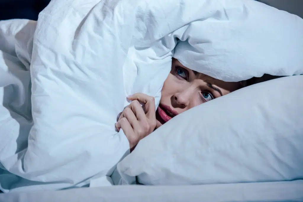 A frightened woman hides under a blanket