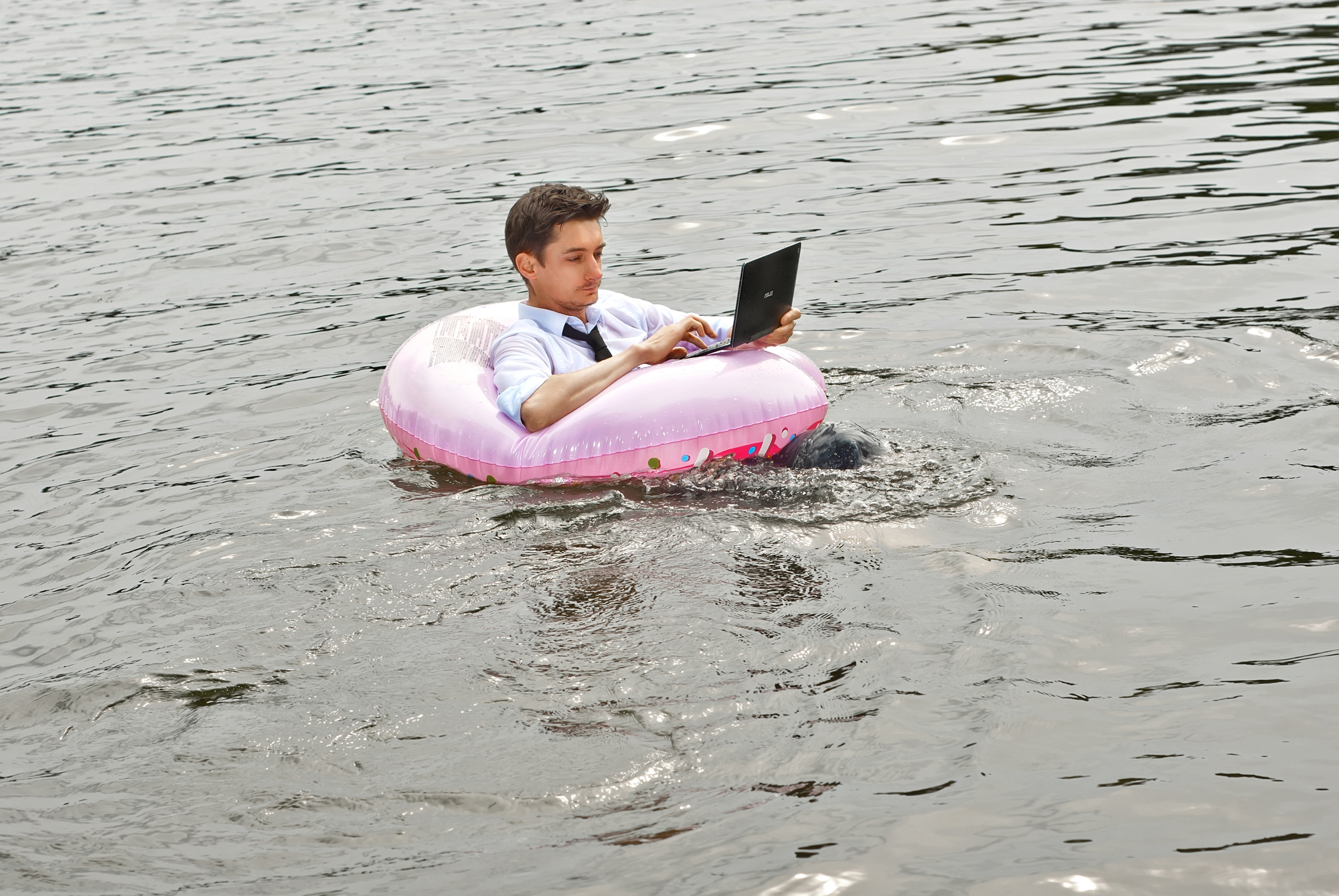 A man in a shirt on a pink inflatable circle. Guy with a laptop swims in the river. The concept of work during vacation, outsourcing and freelance. Place for text and copy space near businessman.