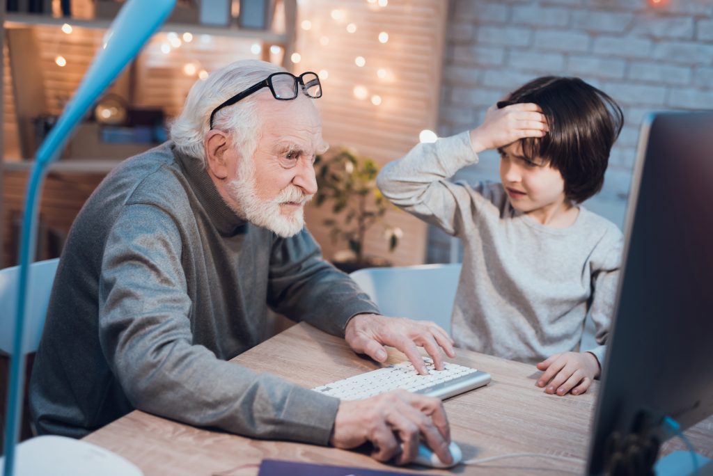 Grandfather and grandson are playing games on computer at night at home. Boy is cheering for granddad.