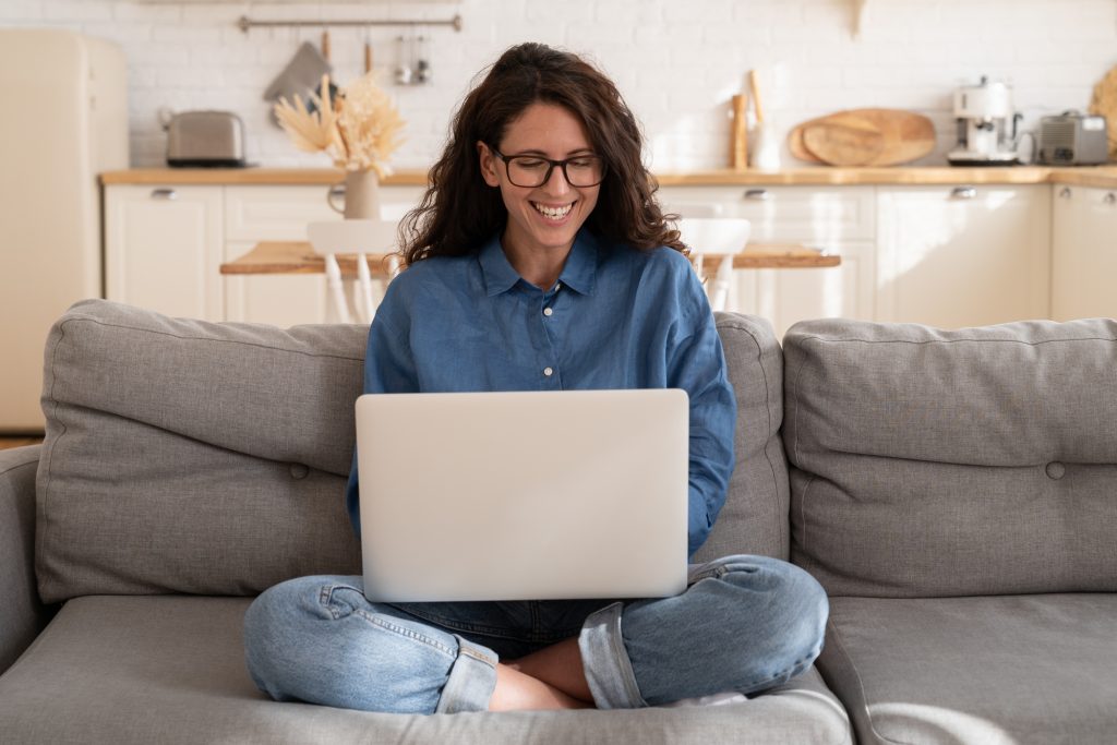 Overjoyed casual girl laugh on sofa with laptop on knees read funny message or watch video online