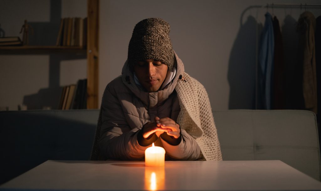 Young man without electricity at home with candle. Shutdown of heating and electricity, power outage, blackout, load shedding or energy crisis