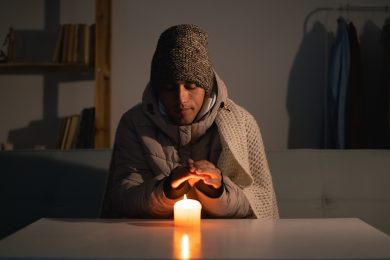Young man without electricity at home with candle. Shutdown of heating and electricity, power outage, blackout, load shedding or energy crisis