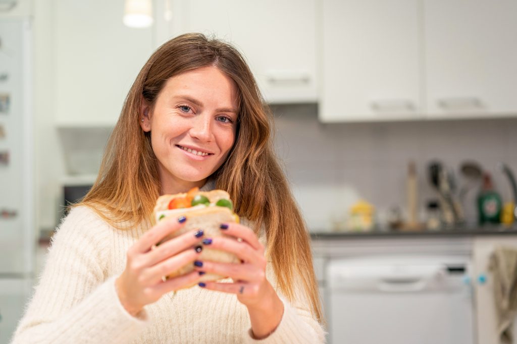 Vegetarian woman cooking a vegetable sandwich in the kitchen at home. finishing preparing it