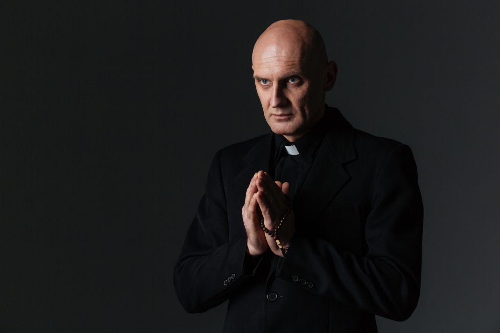 Priest standing and praying over black background