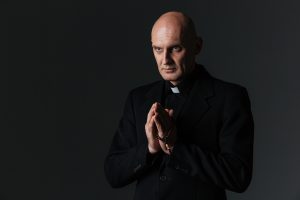 Priest standing and praying over black background
