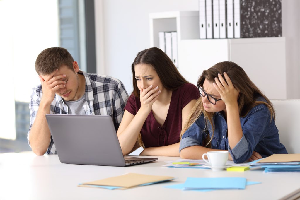 Three worried businesspeople watching on line content in a laptop at office