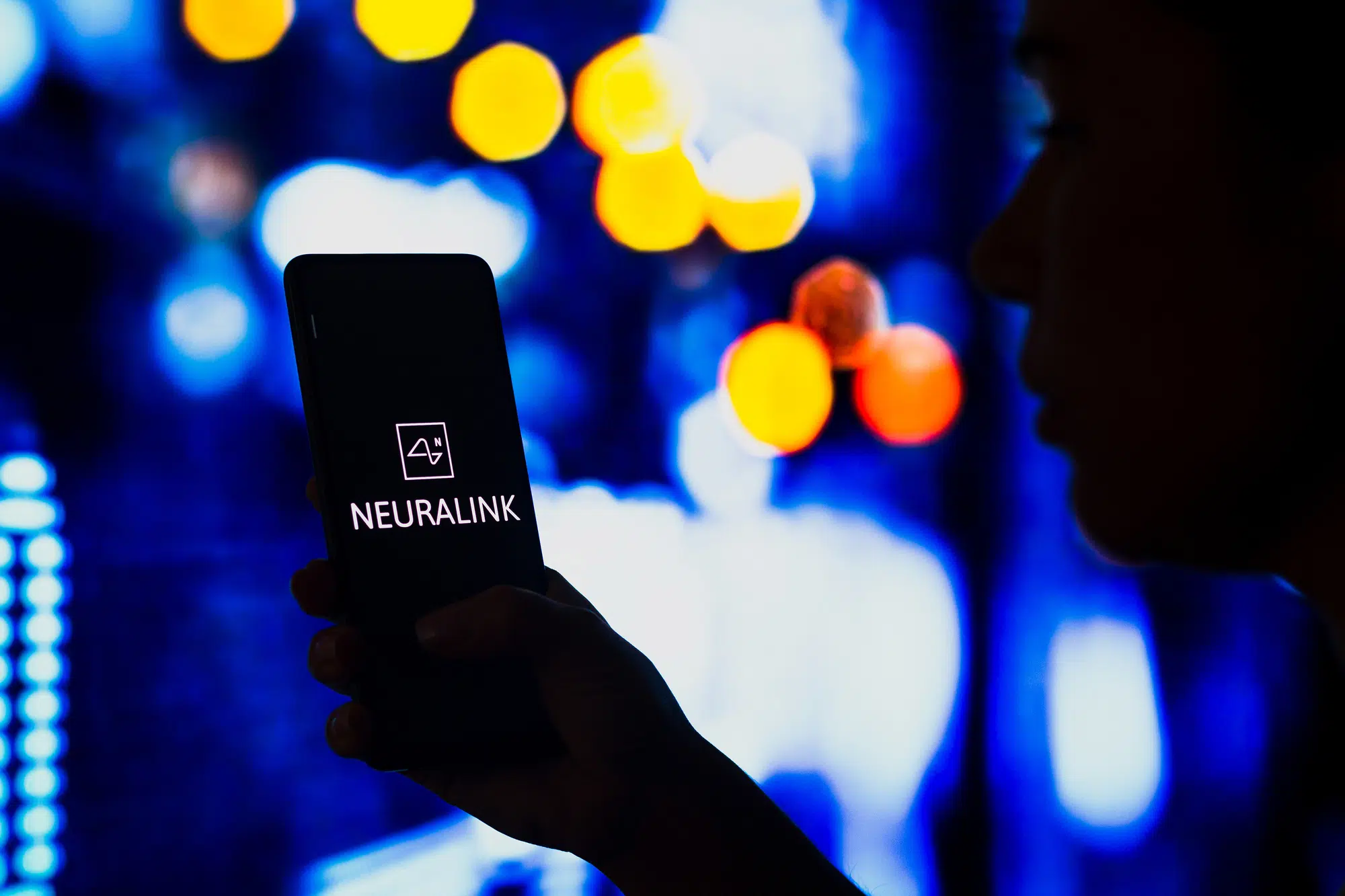 May 2, 2022, Brazil. In this photo illustration, a silhouetted woman holds a smartphone with the Neuralink logo displayed on the screen
