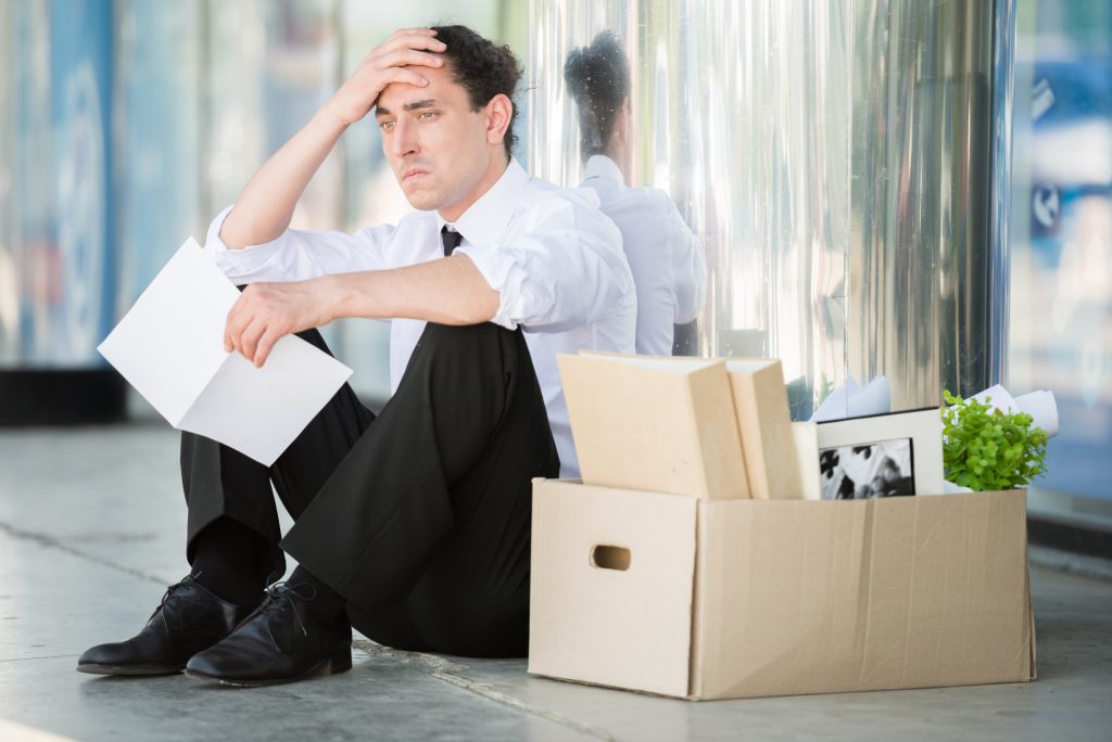Fired frustrated man in suit sitting near office.