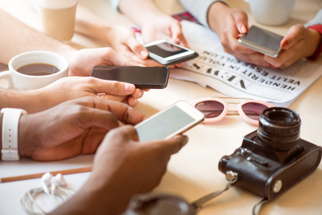 Updated time. Close up of modern people holding mobile phones in their hands and using it while being in a cafe