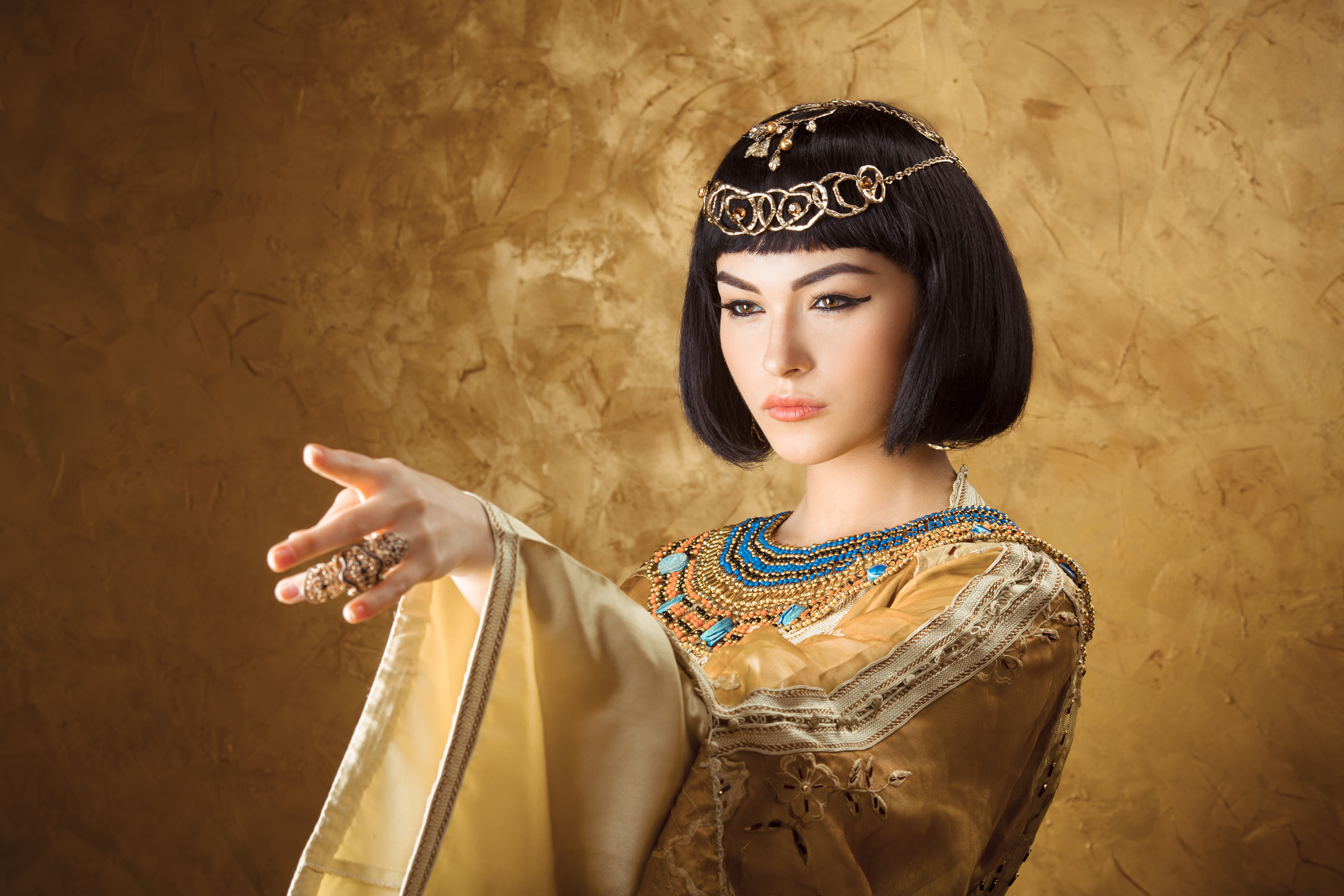 Beautiful Egyptian woman like Cleopatra pointing finger away on golden background