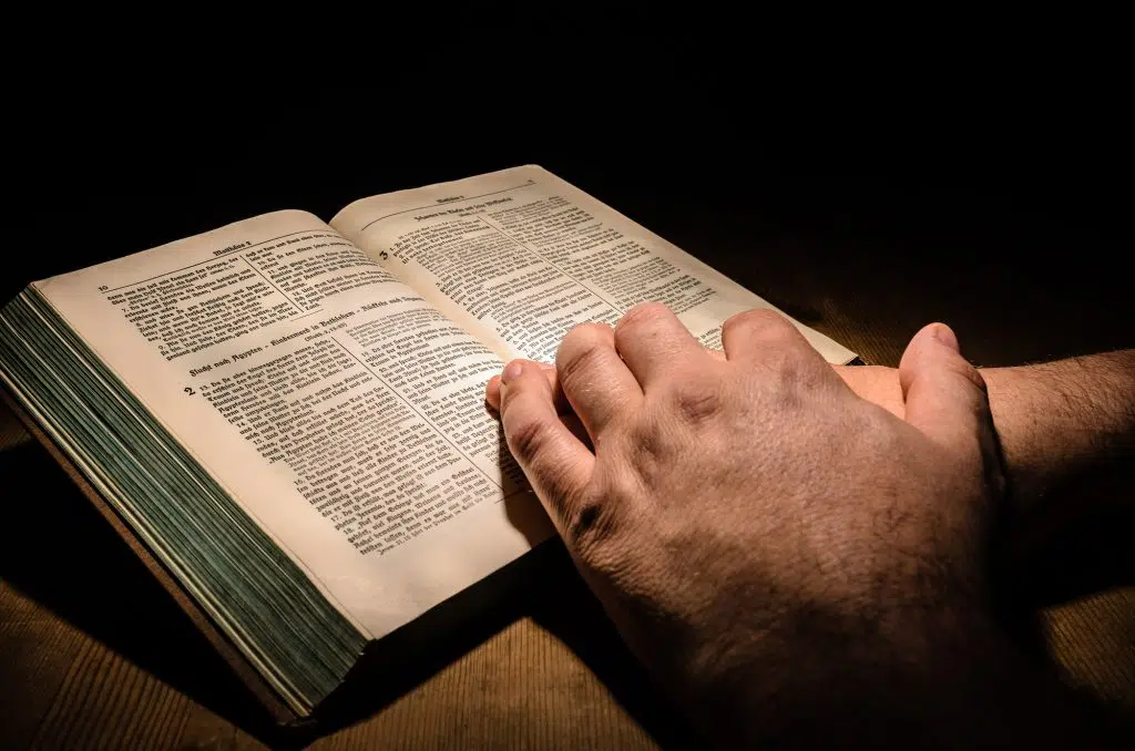 Hands placed on a bible, wooden table with dark background