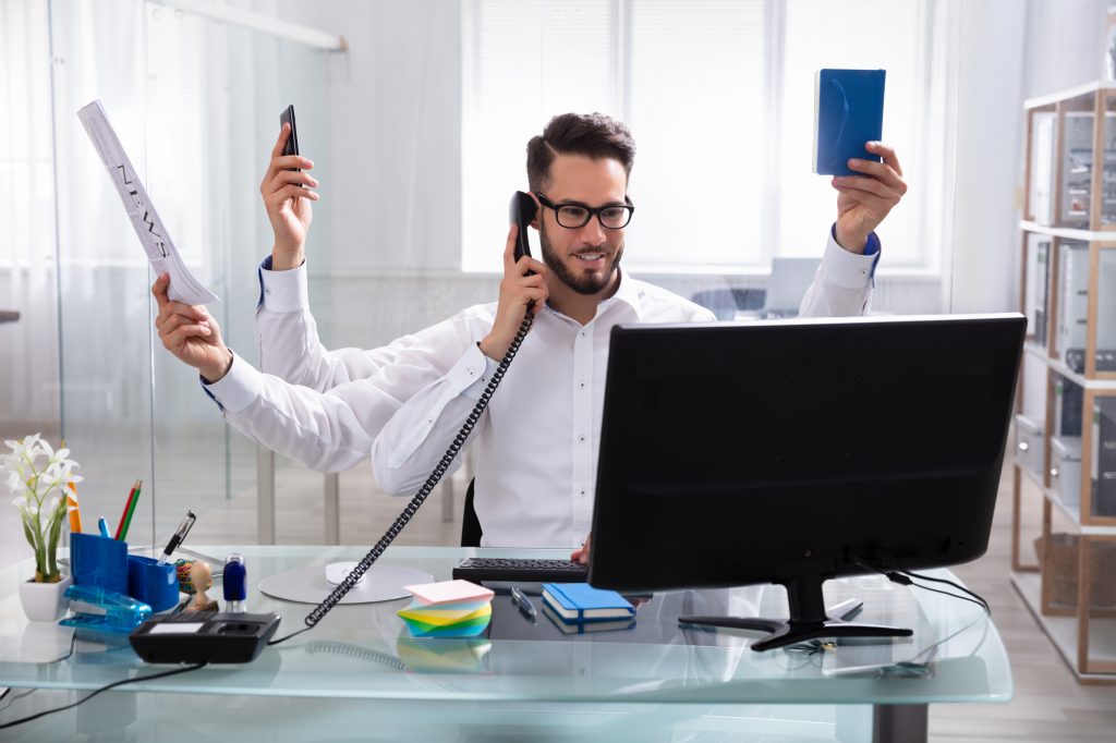 Smiling Young Businessman Doing Multitasking Work At Workplace