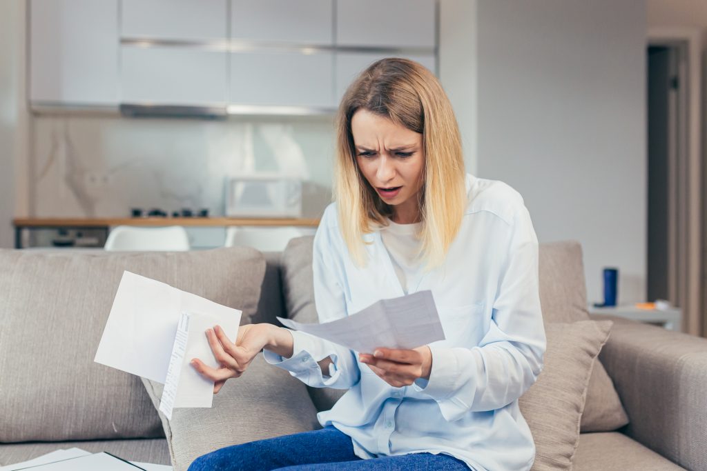 Worried housewife pays inflated bills while sitting on sofa at home, frustrated with work, and monthly income