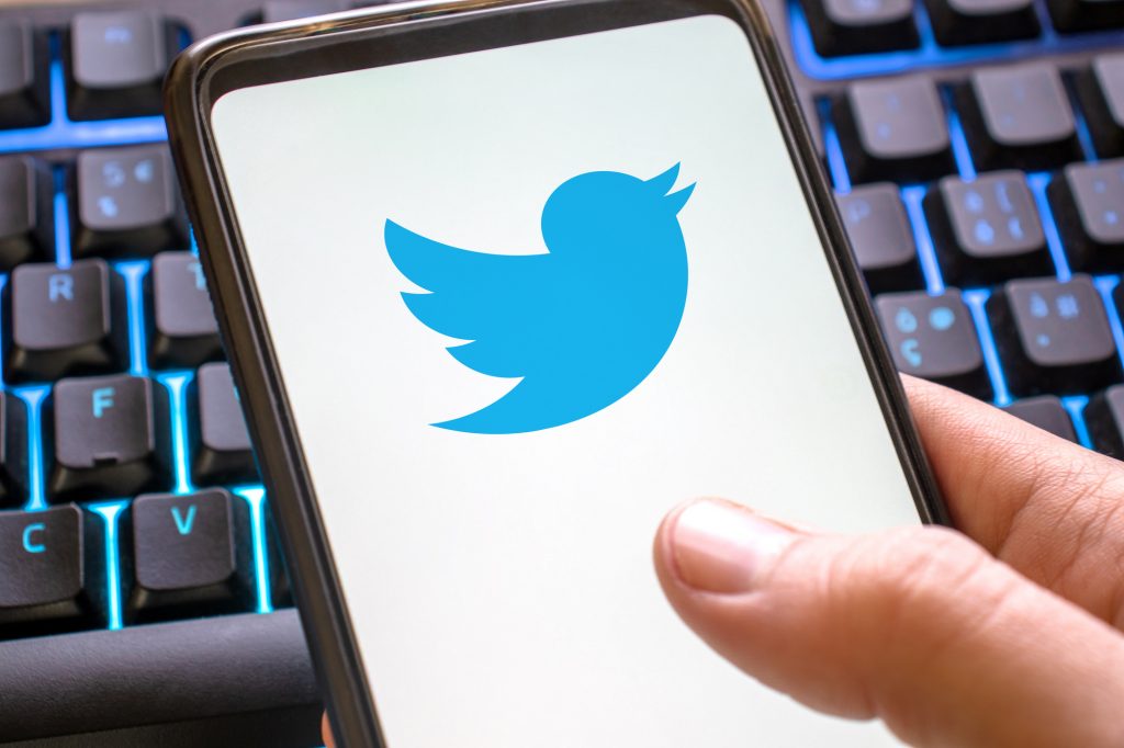 Mobile phone blue twitter icon on display on colored keyboard . Smartphone concept tweet symbol social network