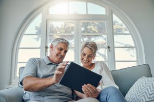 Senior couple tablet, relax smile and living room sofa for social media, email or internet video. Woman man retirement, home happiness with mobile technology and comic social network on web app.