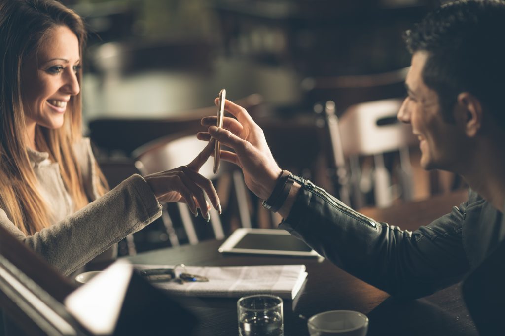Young fashionable couple at the bar using a mobile touch screen phone