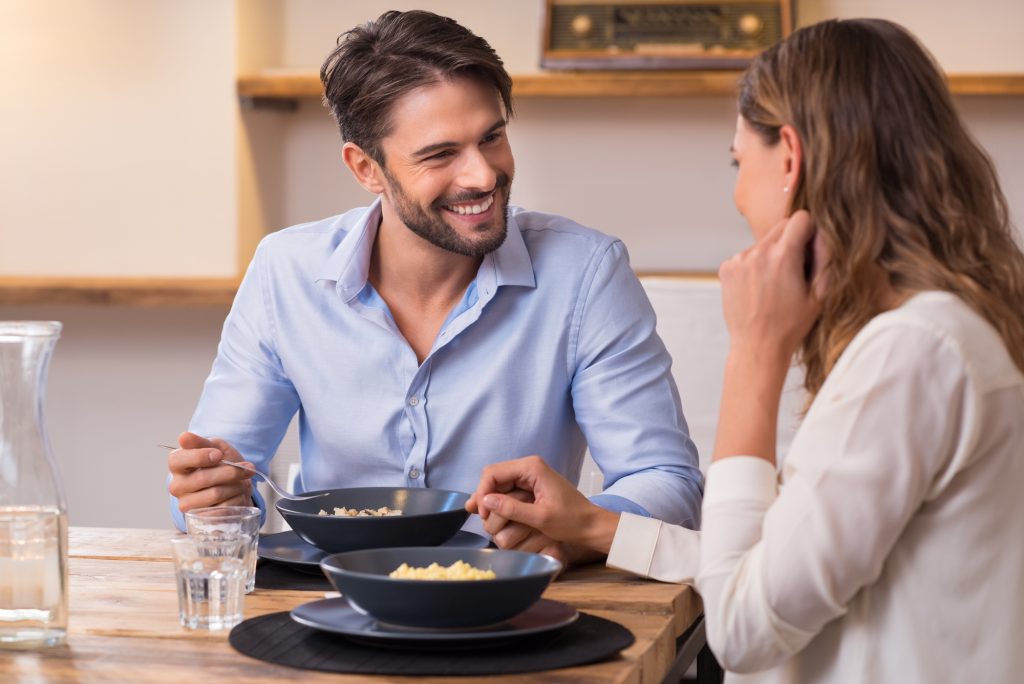 Loving couple looking at each other while having lunch. Close up shot of young man and woman having dinner at home. Happy young couple eating.