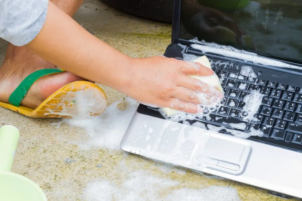 closeup cleaning computer notebook with dish washing soap, technology concept