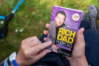 Paris, France - May 3, 2020: Overhead POV view of senior male hand hodling in had reading the iconic book Rich dad and Poor Dad by Robert T Kiyosaki