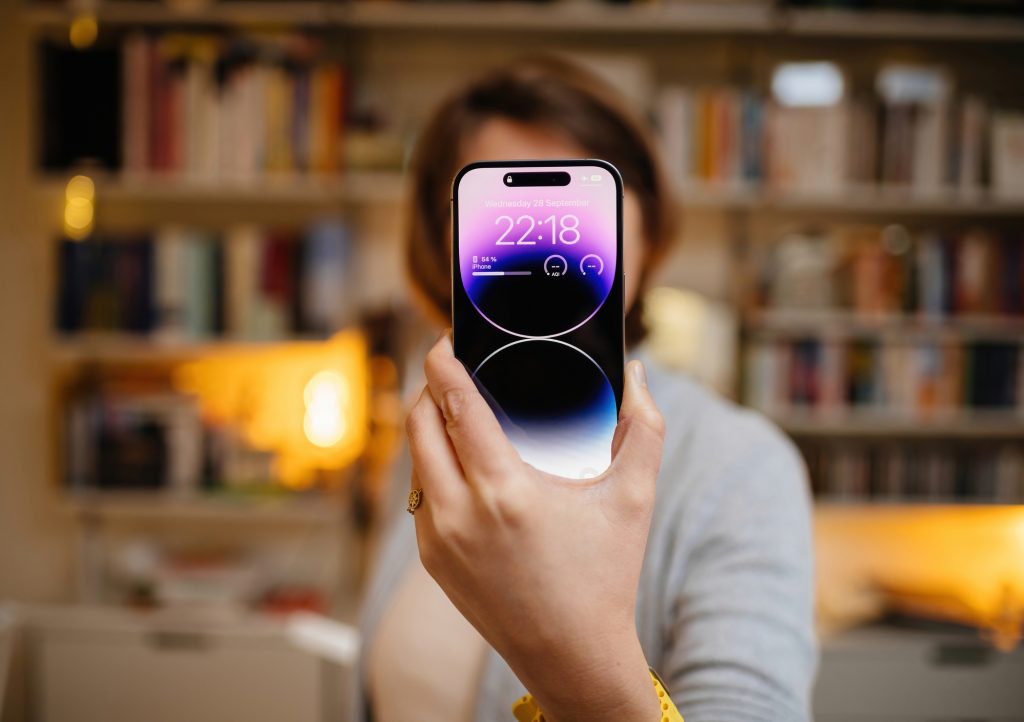 London, United Kingdom - Sept 28, 2022: Woman holding Apple Computers iPhone 14 Pro Max in her hand with living room shelves in background