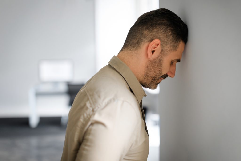 Upset middle aged businessman banging his head against wall in despair looking stressed, having problems at work. Business failure, unsuccessful negotiations, failed job interview concept