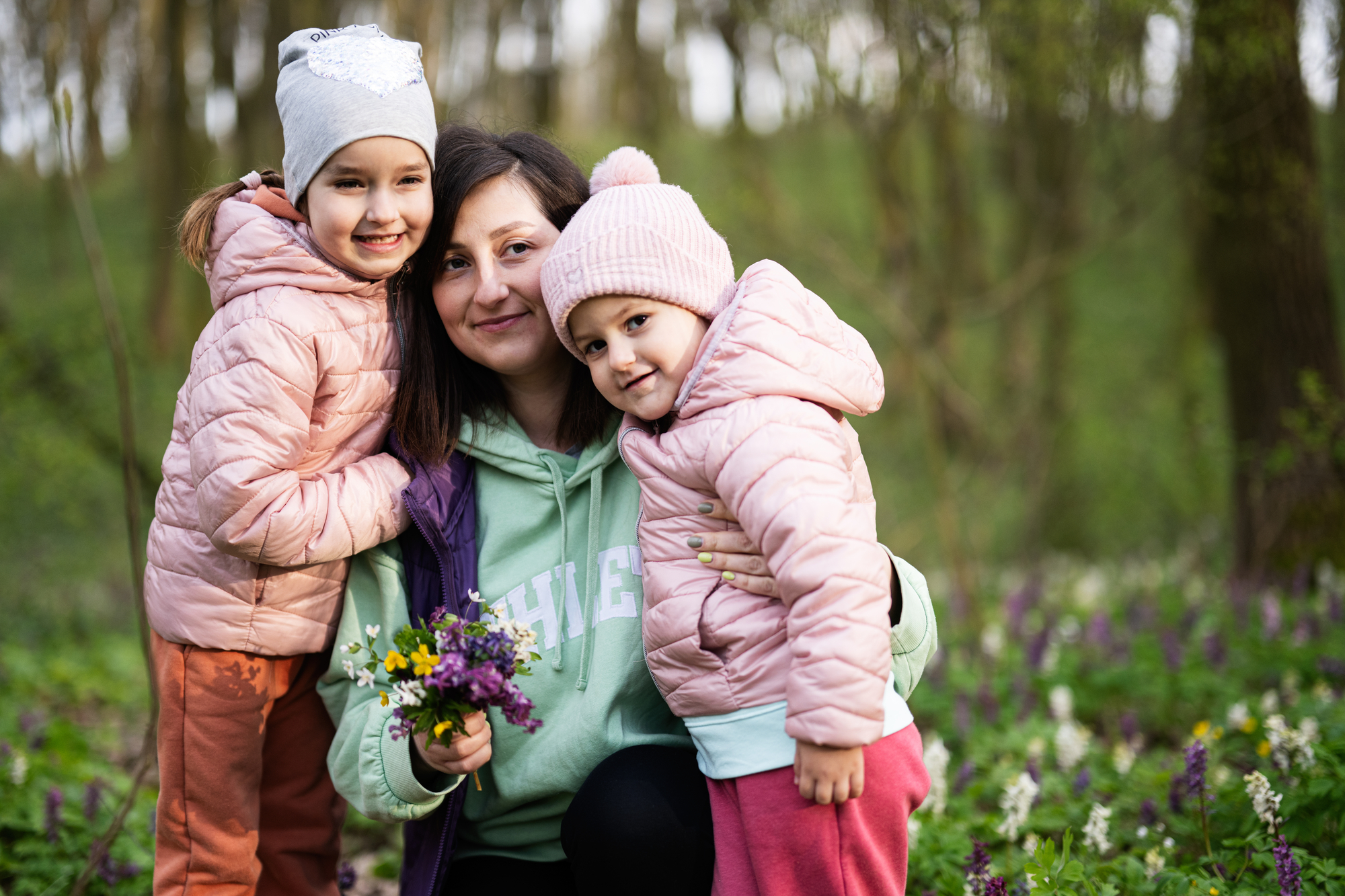 Happy Mother's Day. We love you, mom. Mother with a bouquet of flowers and two daughters in spring blooming forest.