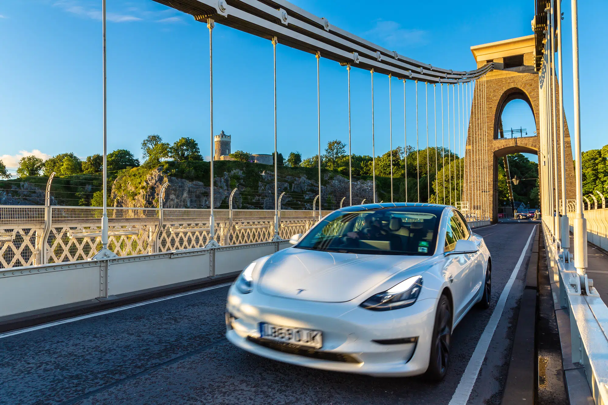 BRISTOL, UK - JUNE 29, 2022: White electric Tesla car at Clifton Suspension Bridge in Bristol at sunset, UK