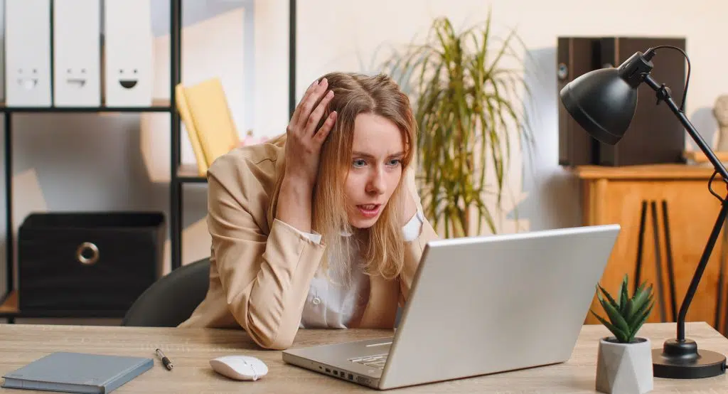 Irritated shocked young business woman while working on laptop, unexpected online website problem, computer virus data loss by hacking. Freelancer feeling mad about broken notebook at office workplace