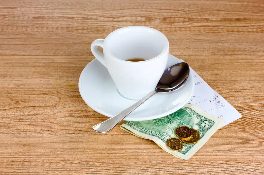 Empty cup of coffee with five dollars tip on wooden background. Ukrainian coins