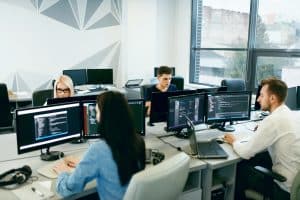 People Working In Modern Office. Group Of Young Programmers Sitting At Desks Working On Computers In It Office. Team At Work. High Quality Image