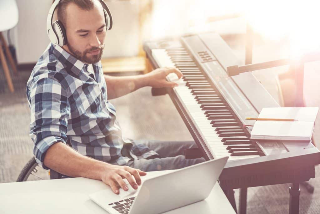 Keen on his work. Confident composer sitting in semi position wearing headphones using laptop while writing new composition