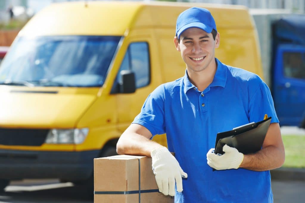 Smiling young male postal delivery courier man in front of cargo van delivering package