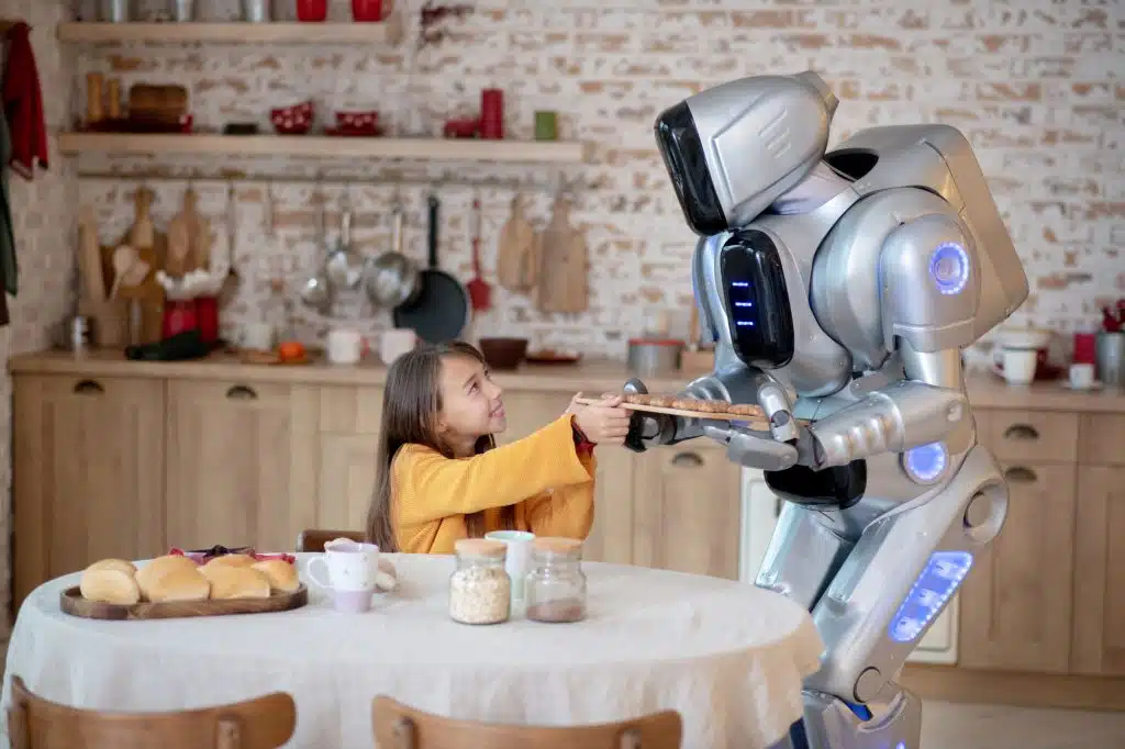 At the table. House robot offering meat balls to the smiling girl at the table