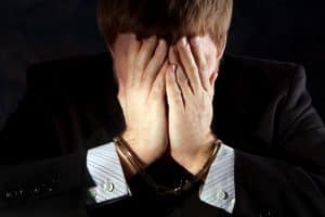 Handcuffs businessman covers his face to hid his identity from shame.
