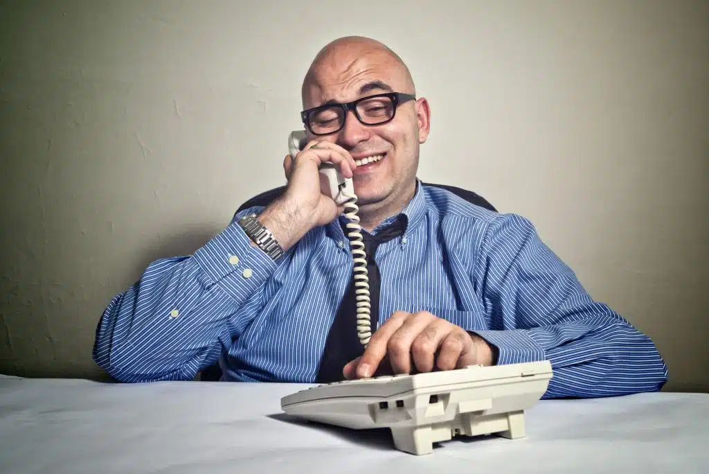 Smiling businessman at office desk with telephone. Wheeler dealer or business crook.